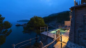 Edificio de piedra con piscina que da a un cuerpo de agua y árboles.