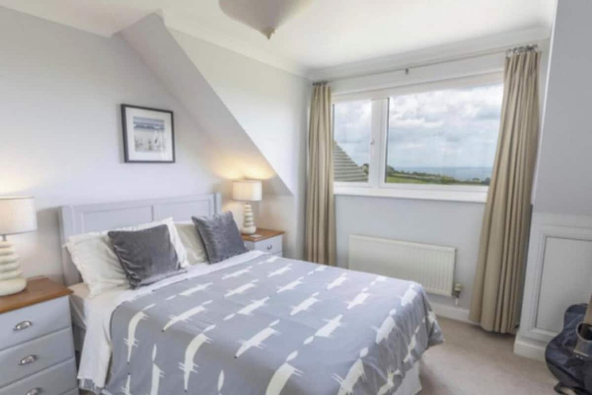 A bedroom with a bed, two bedside tables with lamps, a window with curtains, and a guitar.