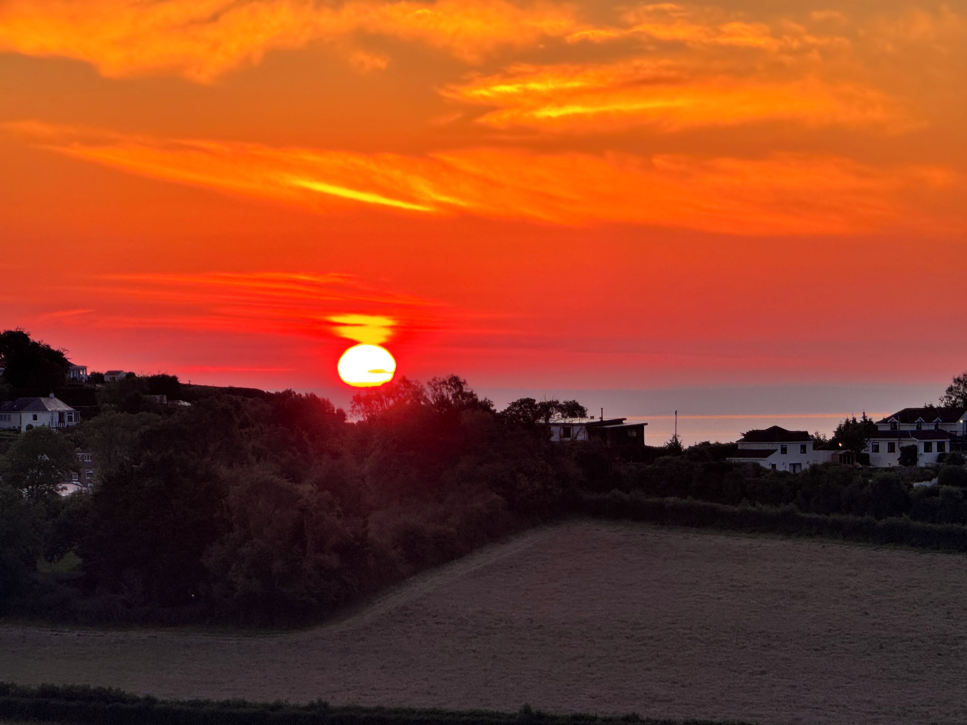A sunset over a residential area with houses and a field.