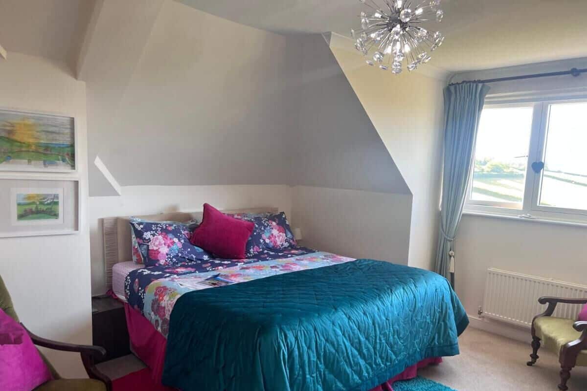 A bedroom with a bed, a chair, a window, and a radiator.