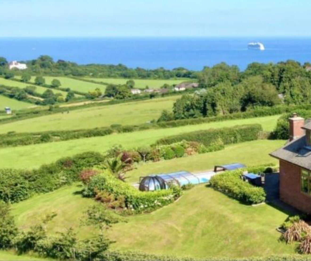 A rural landscape with a house, green fields, and a distant view of the sea.