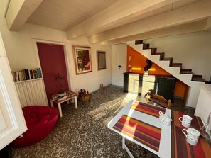 Un'accogliente zona giorno con un sacco di poltrone rosso, un tavolino con tazzine da tè, una libreria e una scala che conduce a una cucina.