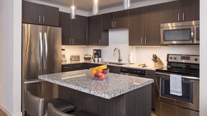 Una cucina moderna con mobili in legno scuro, elettrodomestici in acciaio inossidabile, un piano di lavoro in granito e una ciotola di frutta.