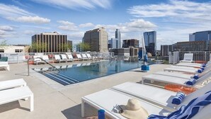 Una piscina sul tetto con poltrona relax, trampolino e panorama urbano sullo sfondo.