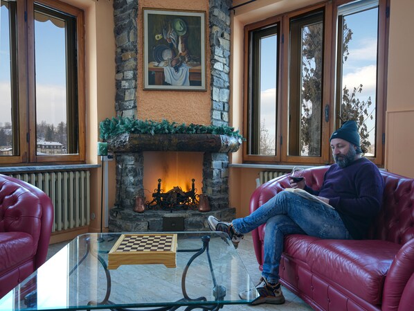 Una habitación acogedora con chimenea de piedra, sofás de cuero rojo y una mesa de centro de cristal con un tablero de ajedrez.