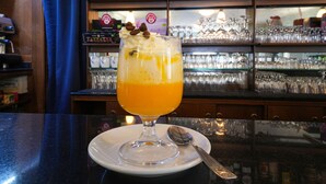 A bar setting with a glass of orange juice and whipped cream, a spoon, and a bottle of liquor on the shelf. - Hotel Skilift (Frabosa Soprana)