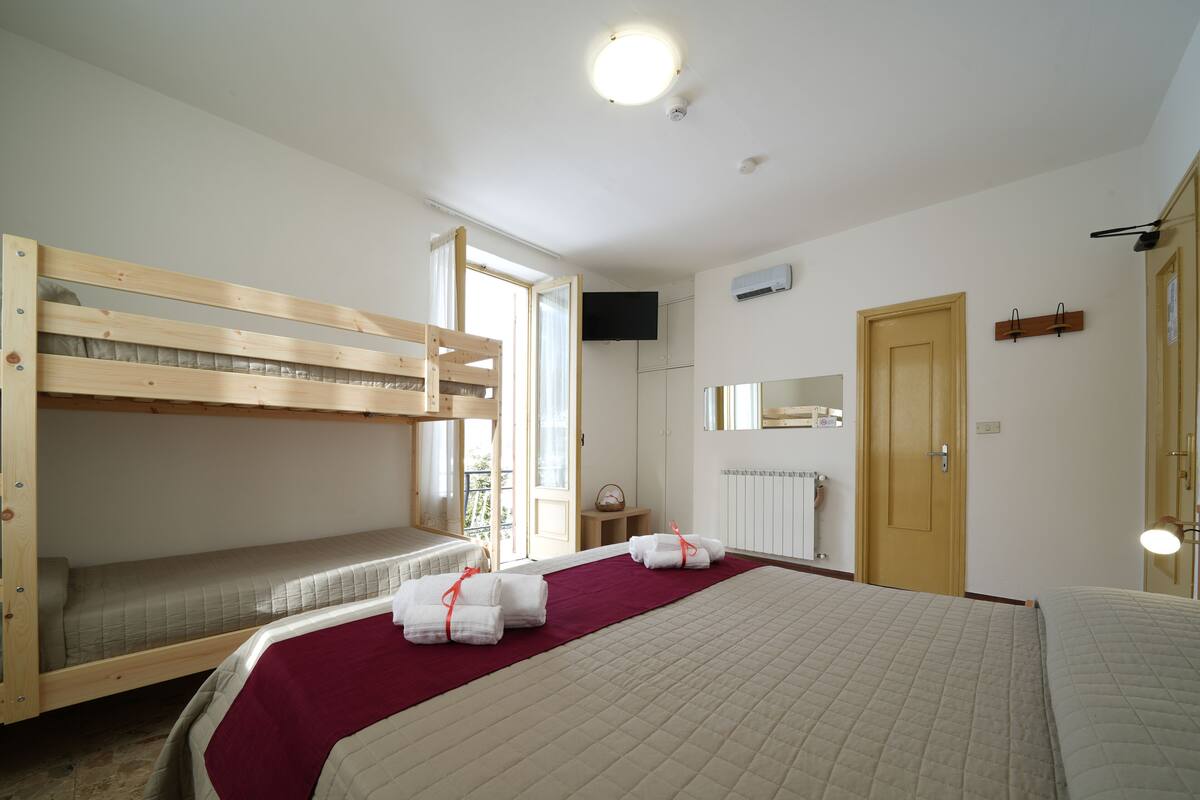 A room with bunk beds, a large bed, a window, a door, and a mirror.