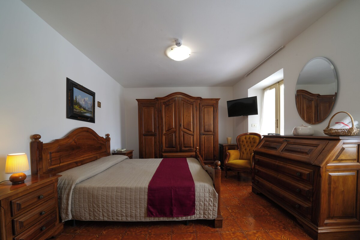 A bedroom with a bed, wooden wardrobe, a television, and a mirror.