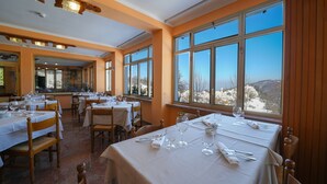 A restaurant with multiple tables set for dining, large windows with a view of a snowy landscape, and wooden ceiling beams. - Hotel Skilift (Frabosa Soprana)