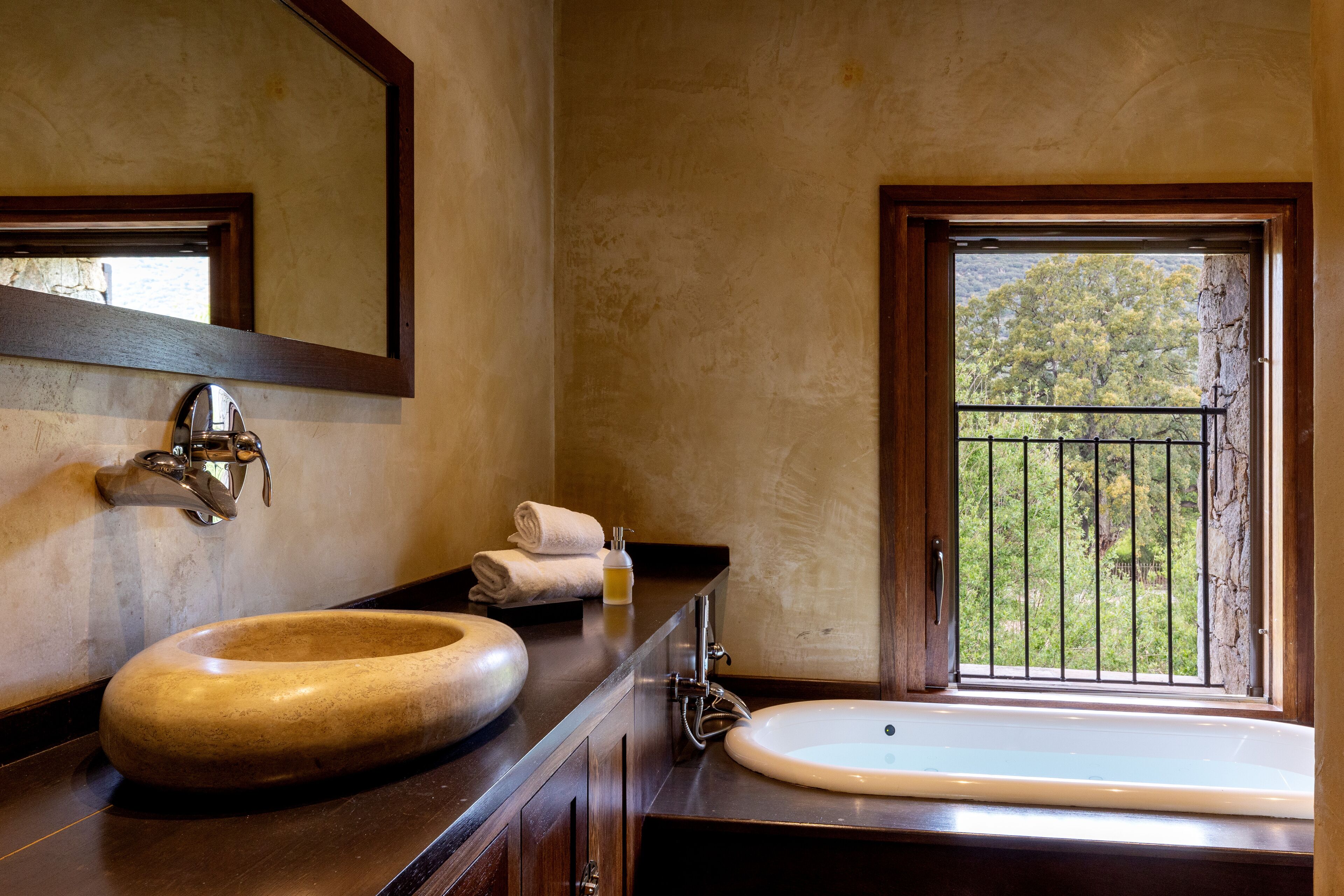 Un baño con lavamanos de madera, un espejo y una ventana con vistas a la vegetación.