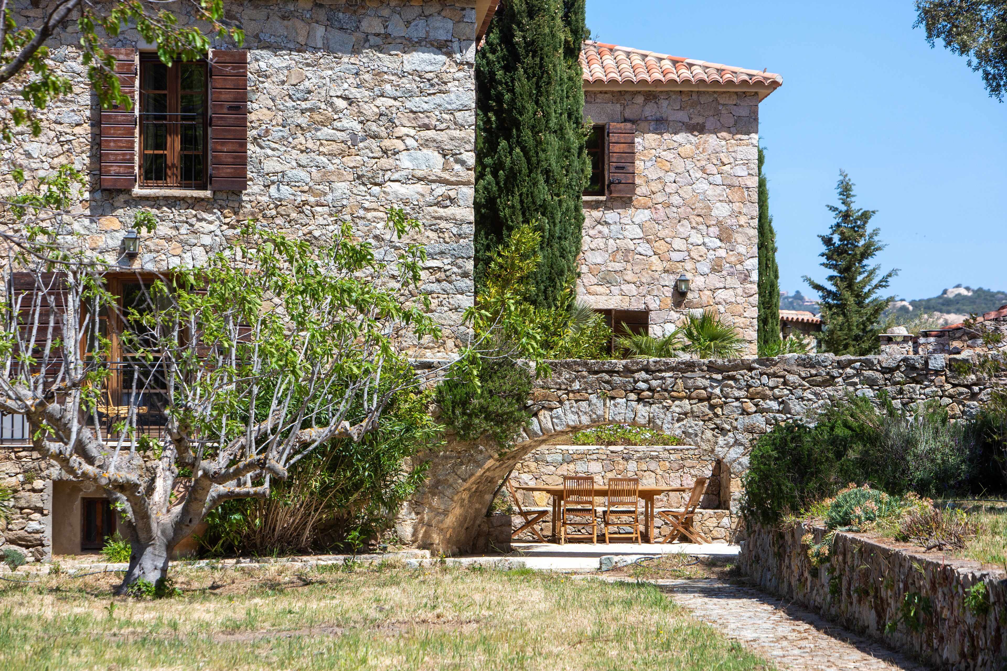 A stone house with a stone archway leading to a patio area with a table and chairs.