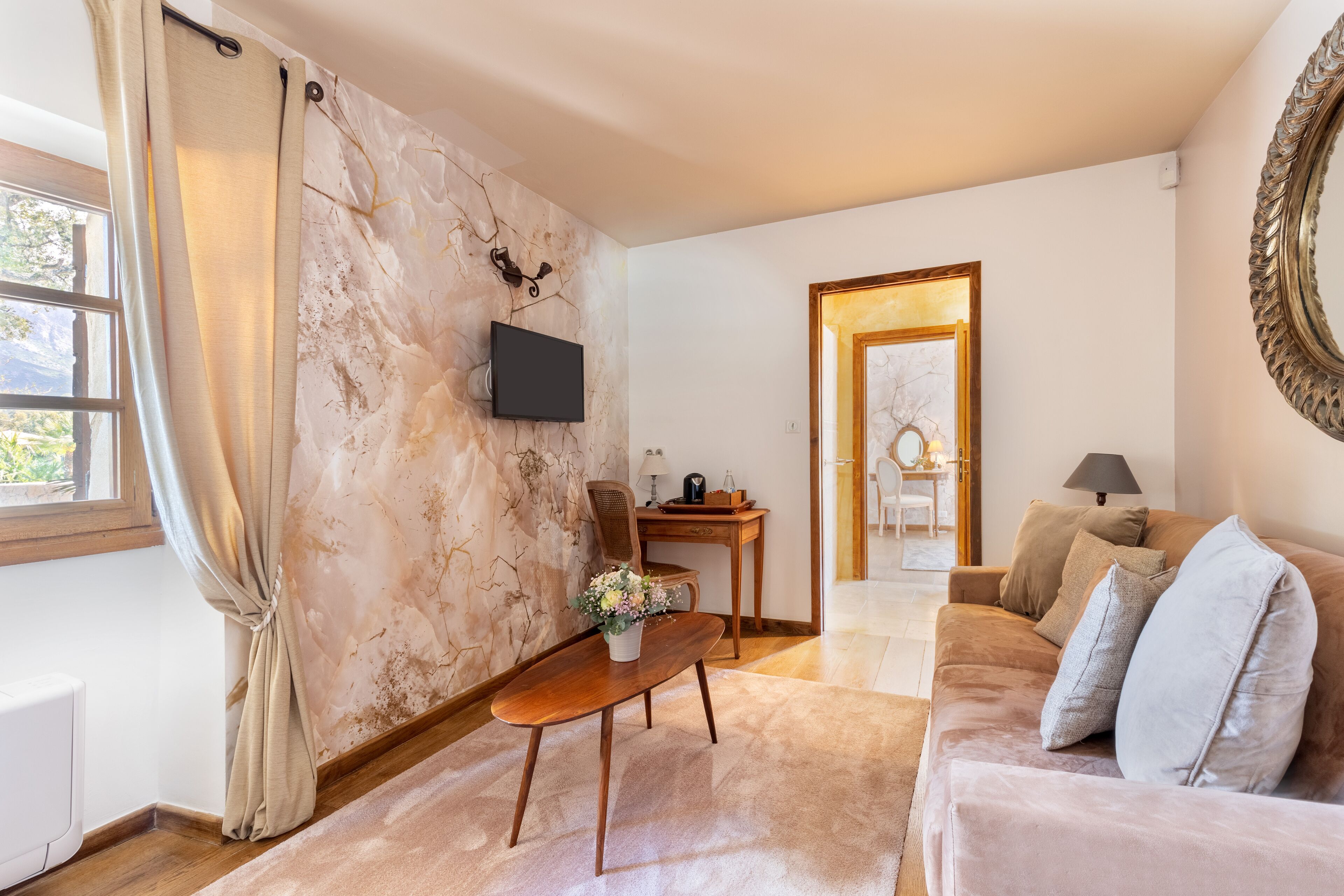Een woonkamer met een marmeren wand, een flatscreen televisie, een houten salontafel, een beige bank en een houten bureau met stoel.