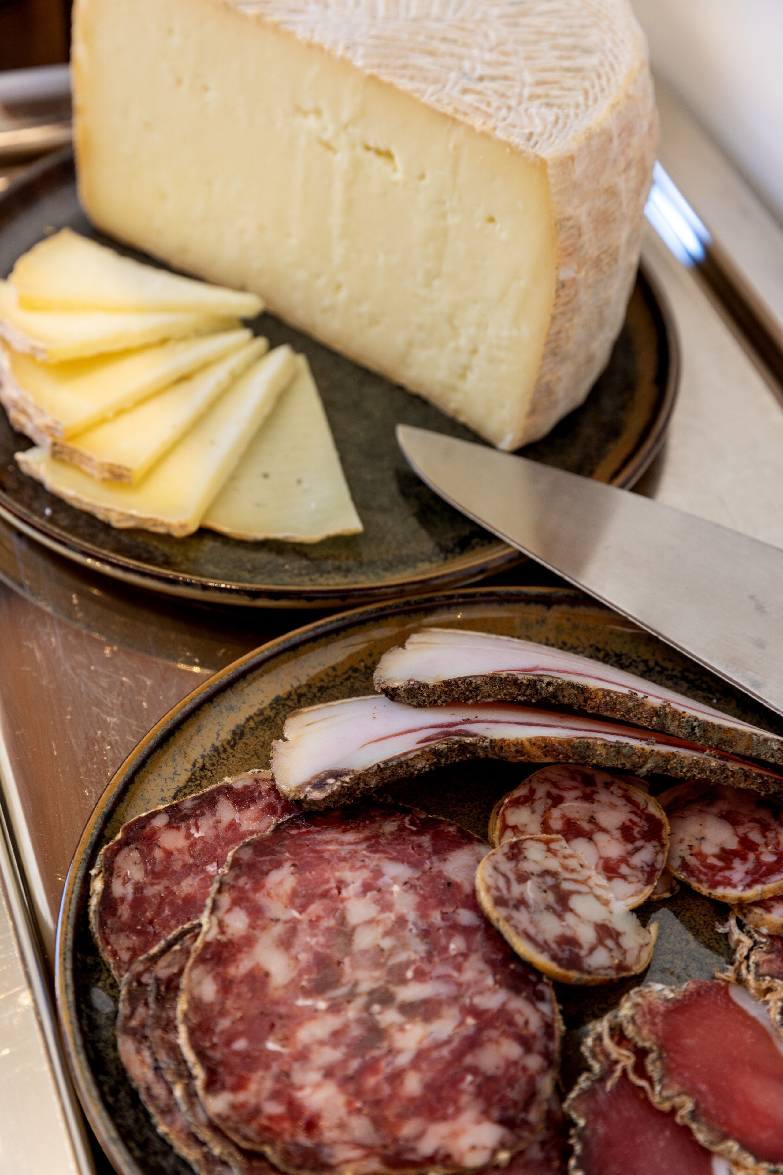 A cheese wheel and sliced meats on plates.