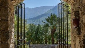 Un arc de pedra condueix a un pati empedrat, amb vista a muntanyes i palmeres.