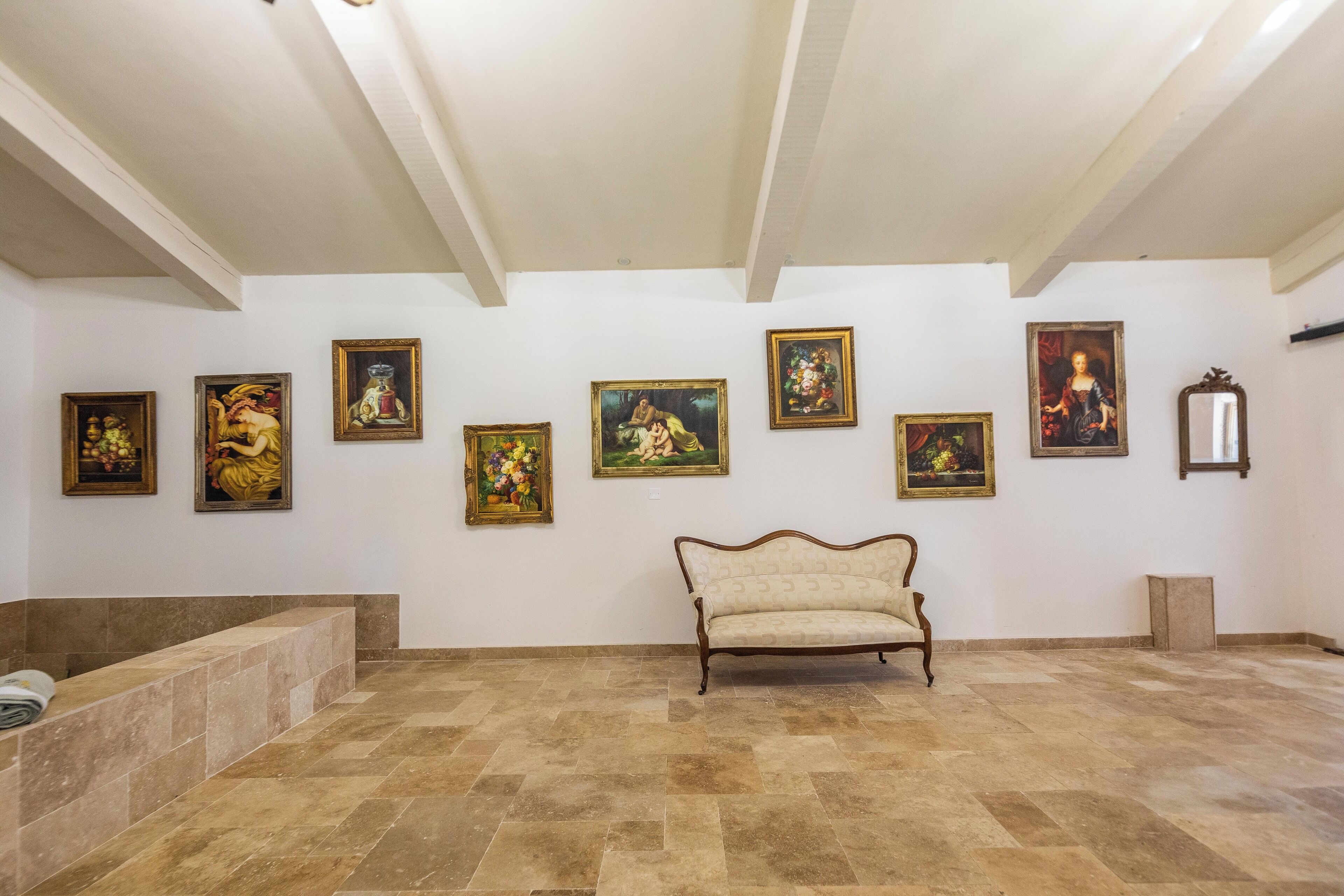 Une galerie avec un canapé, un sol carrelé et divers tableaux encadrés accrochés aux murs.