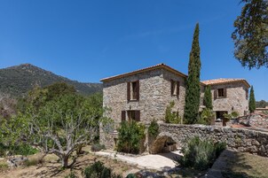 Um edifício de pedra com telhado de cerâmica, rodeado por árvores e uma montanha ao fundo.