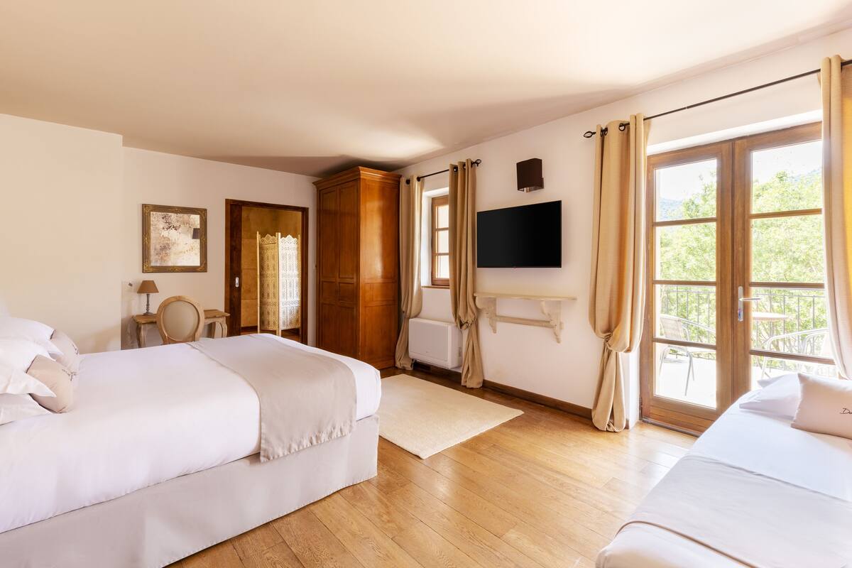 Ein Hotelzimmer mit zwei Betten, einem Fernseher, einem Holzschrank und einem Balkon mit Gartenmöbeln.
