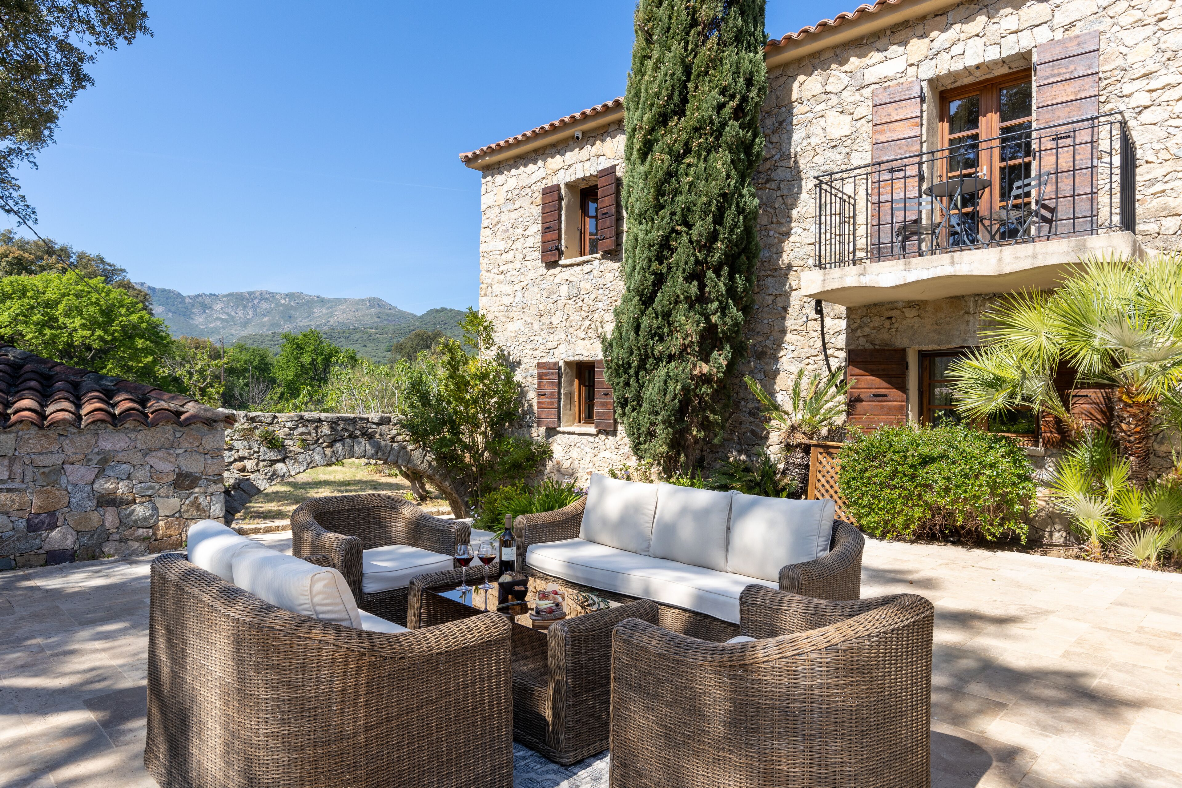 A stone building with a balcony, wicker furniture, and a stone wall.