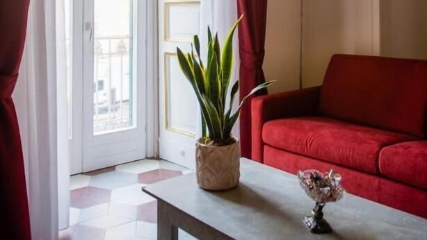 A room with a red sofa, a table with a plant, and a lamp. - ForiArt Relais (Naples)
