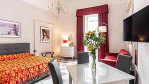 A hotel room with a bed, a dining table, a TV, and a window with curtains. - ForiArt Relais (Naples)
