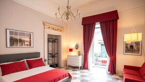 A hotel room with a bed, a dresser, a chair, a chandelier, and a view of the outside. - ForiArt Relais (Naples)