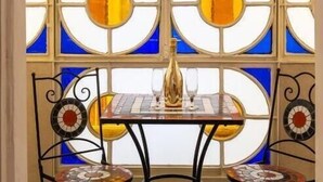 A dining table with two chairs, a bottle, and a glass. The table is set against a window with stained glass panes. - ForiArt Relais (Naples)