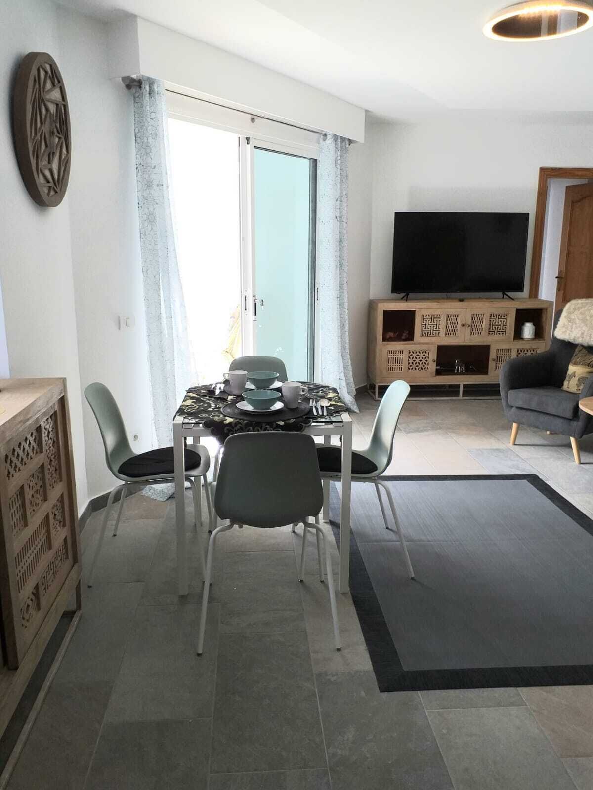A modern living room with a dining area, a flat-screen TV, and a sofa.