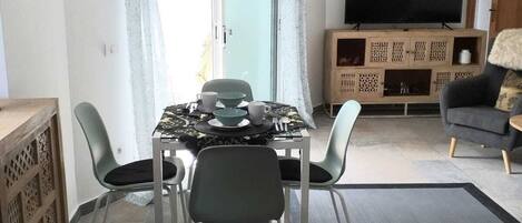 A modern living room with a dining area, a flat-screen TV, and a sofa.