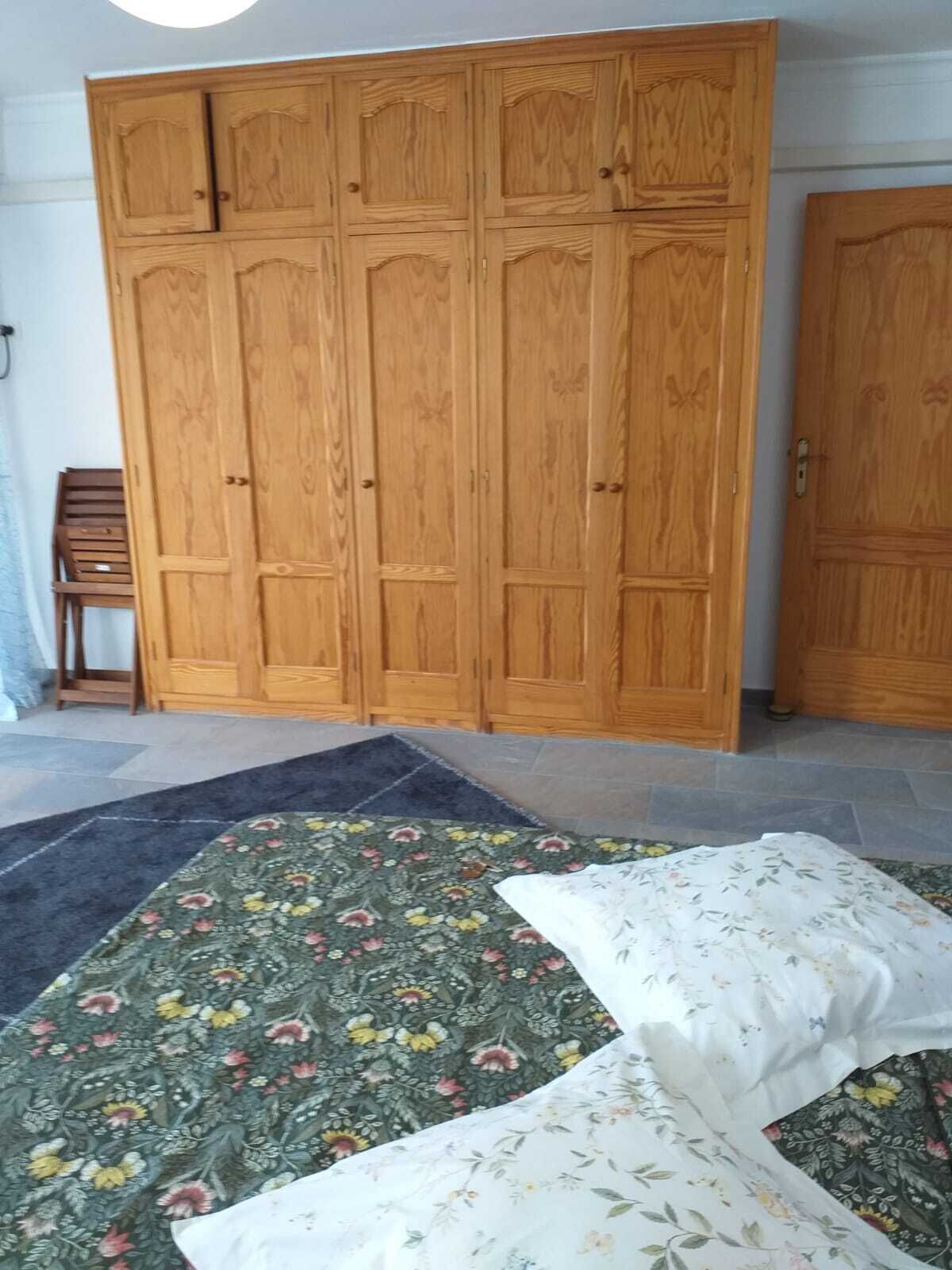 Ett rum med en stor garderob i trä, en matta med blommönster och en säng med ett blommigt överkast.