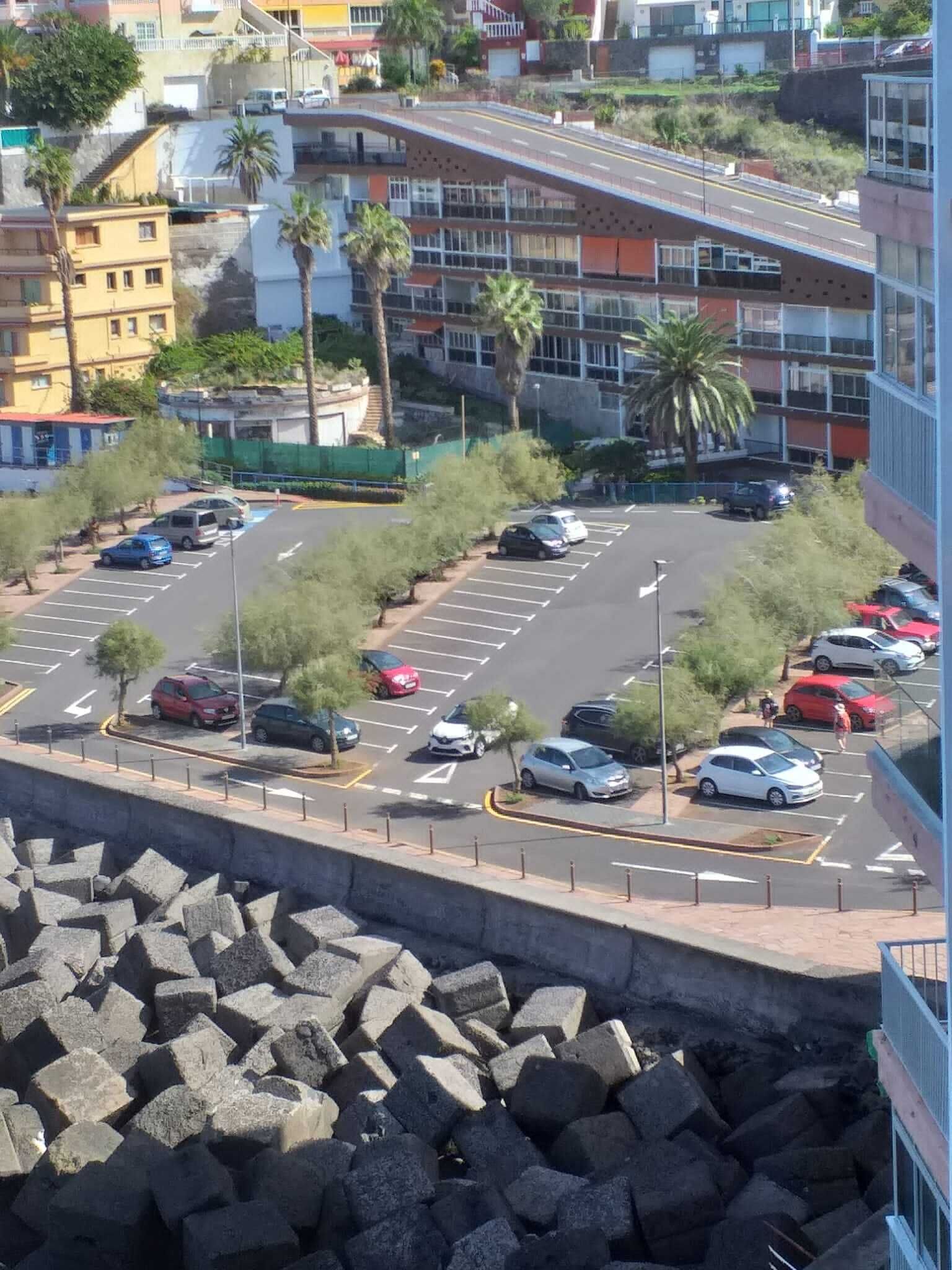Un parking avec plusieurs voitures, un chemin piétonnier et des bâtiments en arri ère-plan.