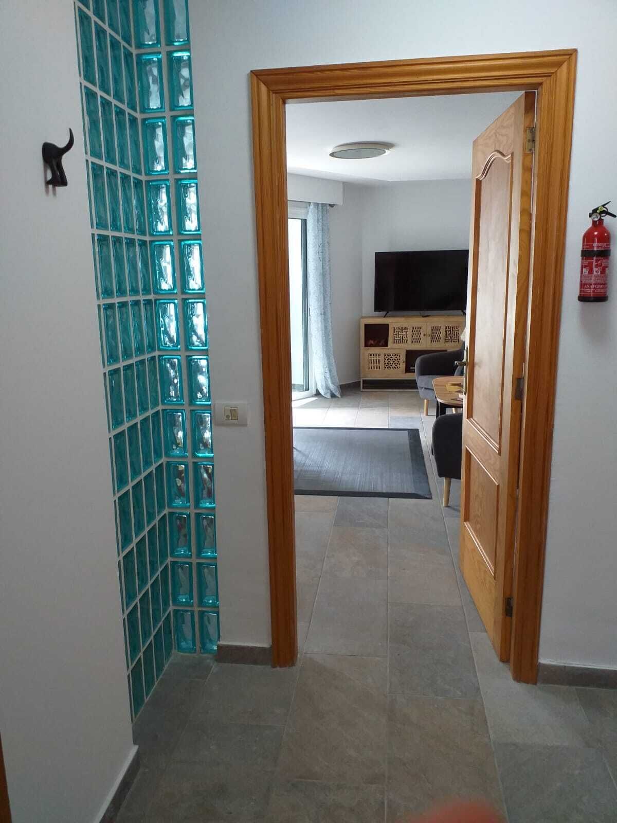 Un pasillo con una puerta de madera que da a una sala de estar con televisor, sofá y un mueble de madera.