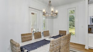 Zona pranzo con tavolo bianco, sedie in vimini e lampadario.