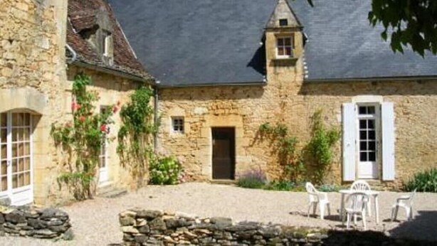 A stone building with a courtyard, a small tower, and white shutters on the windows.