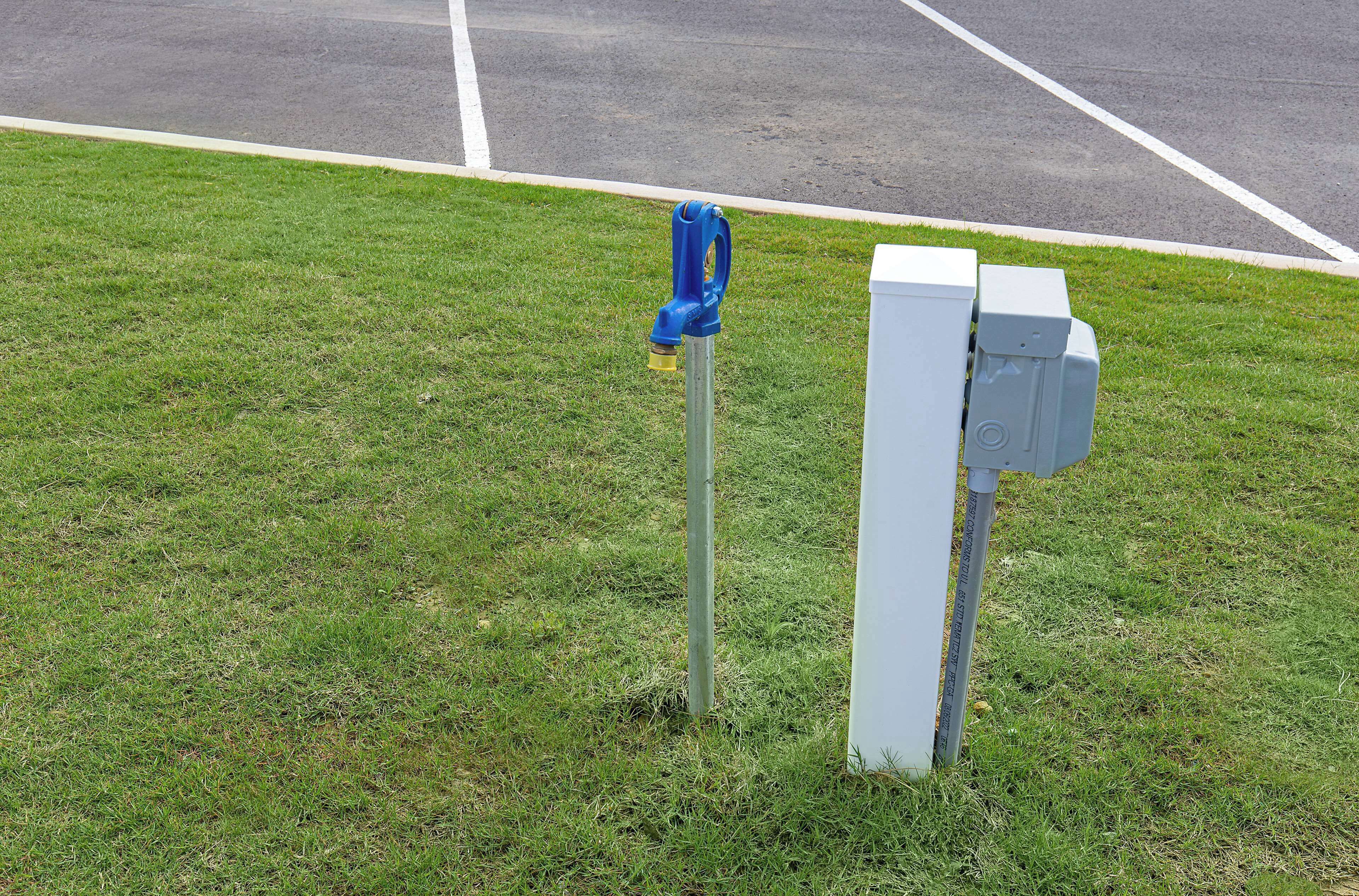 A parking lot with a blue fire hydrant and two white electrical boxes on a grassy area.