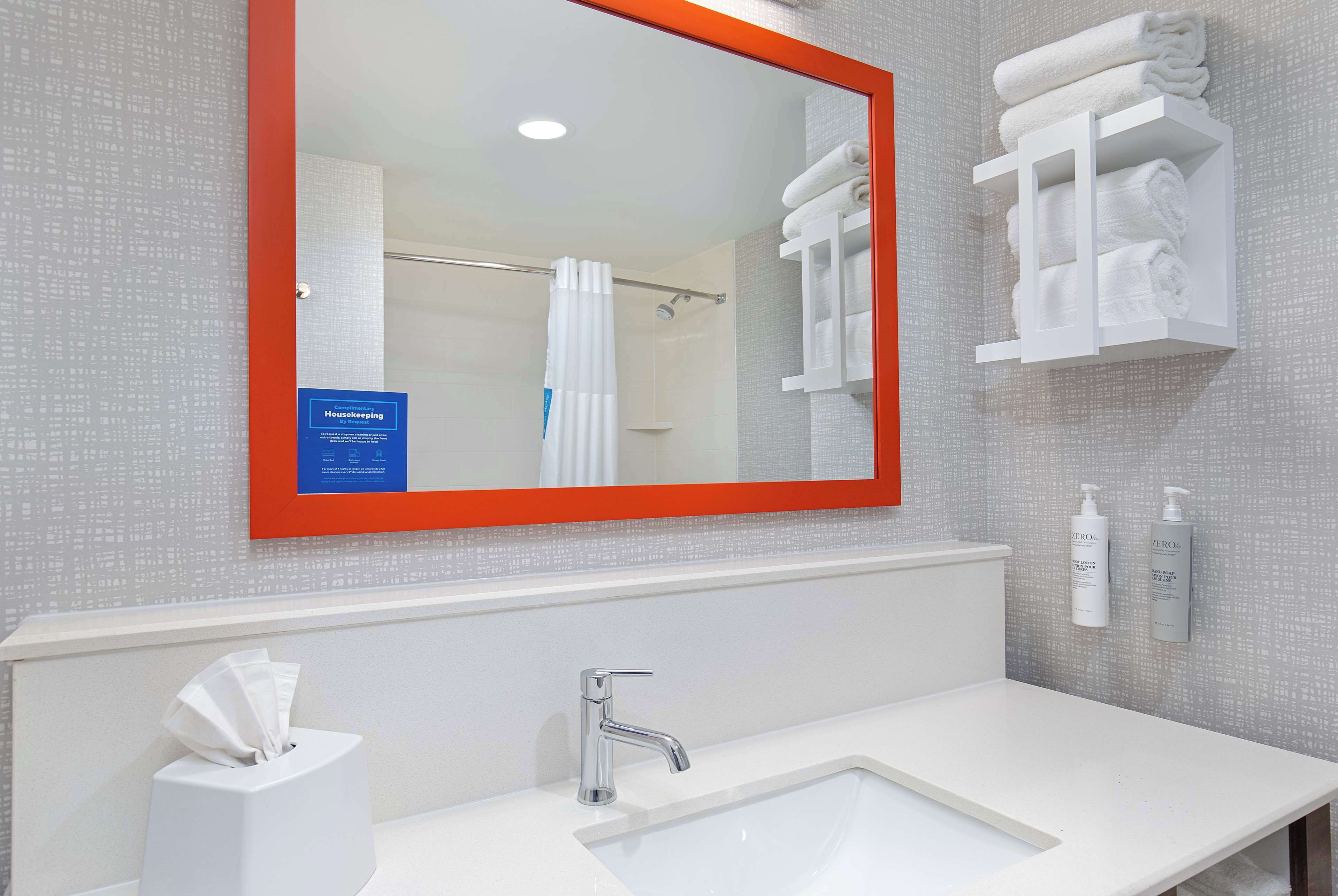A bathroom with a white sink, a mirror with an orange frame, and a towel rack with folded towels.