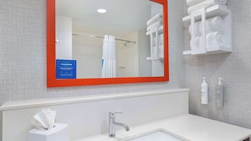 A bathroom with a white sink, a mirror with an orange frame, and a towel rack with folded towels.