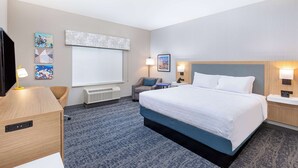 Hotelkamer met een groot bed, een bureau met lamp, een stoel, een projectiescherm en kunstwerken aan de muur.