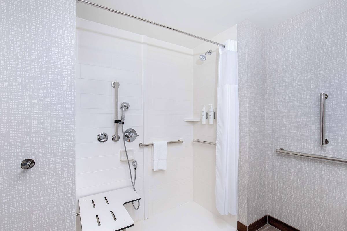 Une salle de bain moderne avec une douche à l’italienne en verre, des murs recouverts de carreaux blancs et un porte-serviettes blanc.