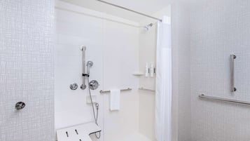Un baño moderno con cabina de ducha de vidrio, paredes con azulejos blancos y un perchero blanco.