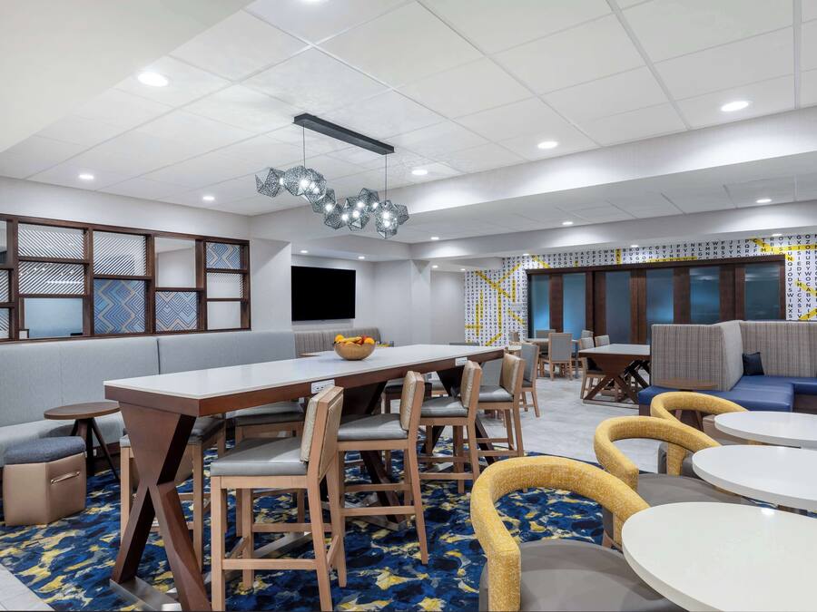 A modern hotel lobby with a long dining table, comfortable seating, and a patterned wall.