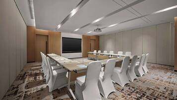 A conference room with a long table, white chairs, a projector screen, and a carpeted floor.