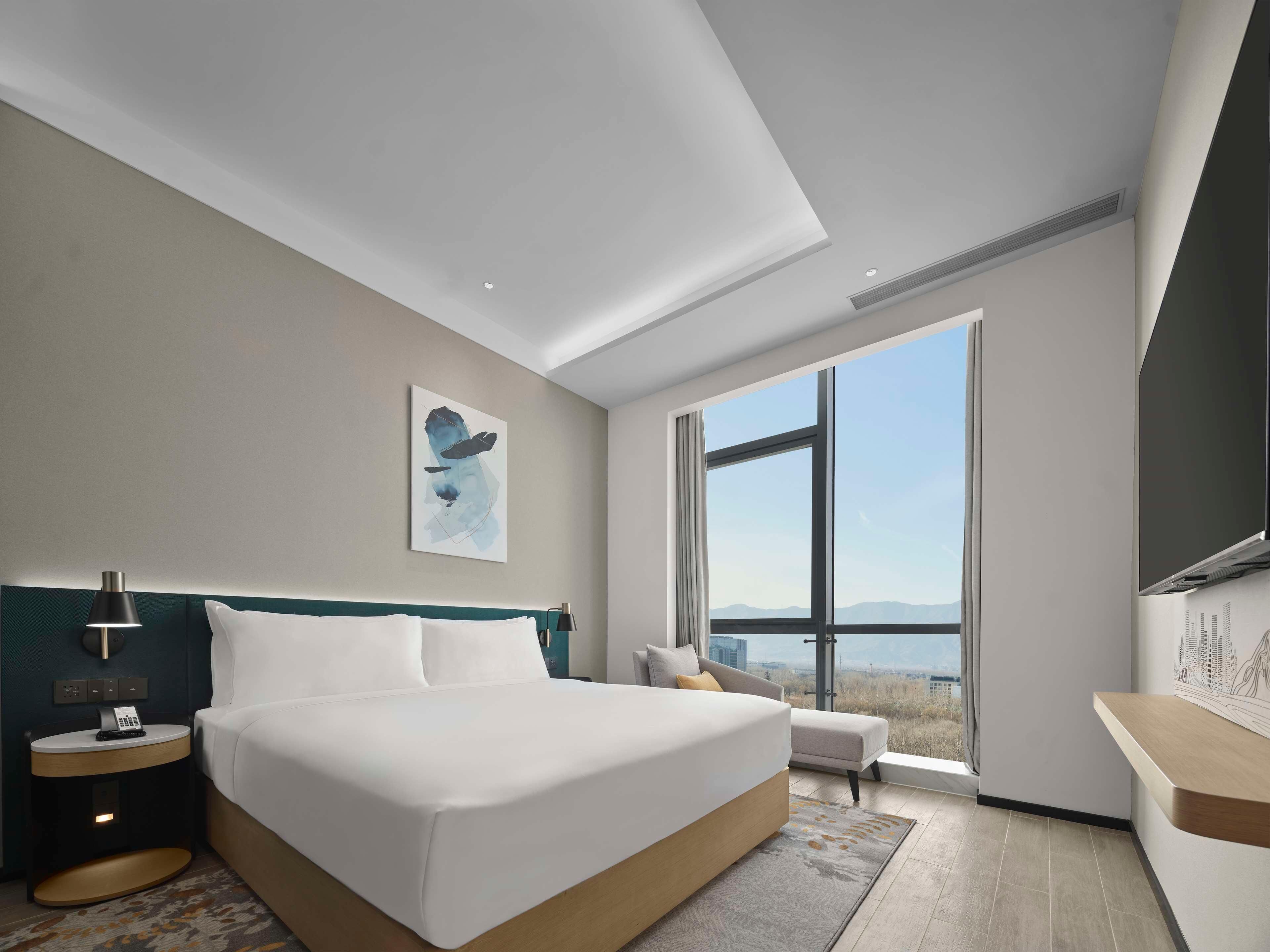 Habitación de hotel moderna con una cama grande, un escritorio, una silla, un cuadro y vistas a las montañas.