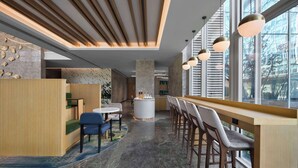 Una zona de bar moderna con una barra alargada, taburetes y un área de estar con una mesa redonda y sillas.