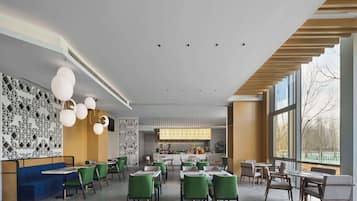 Un restaurant moderne avec des sièges aux couleurs vertes et bleues, un espace cuisine et de grandes fenêtres offrant une vue dégagée.