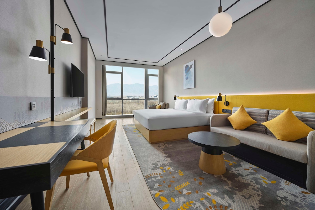 Habitación de hotel moderna con una cama grande, un sofá, una zona de comedor y un televisor montado en la pared.
