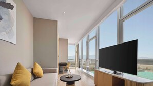 Una sala de estar moderna con un televisor grande, un sofá con cojines, una mesita y vistas a montañas a través de amplios ventanales.