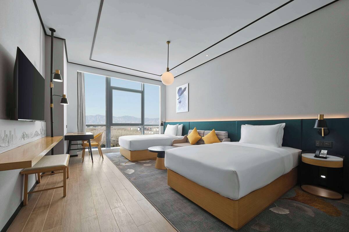 Habitación de hotel moderna con una cama grande, un escritorio y una silla. Se ve una vista de montañas por la ventana.