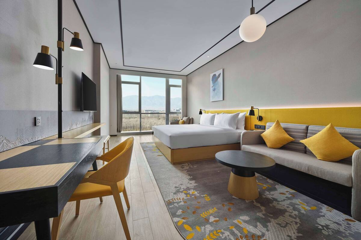 Una habitación de hotel moderna con cama, sofá, mesa de comedor, sillas y televisión.