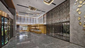Un vestíbulo espacioso con mostrador de recepción, luminarias modernas y un panel decorativo con motivos de hojas.