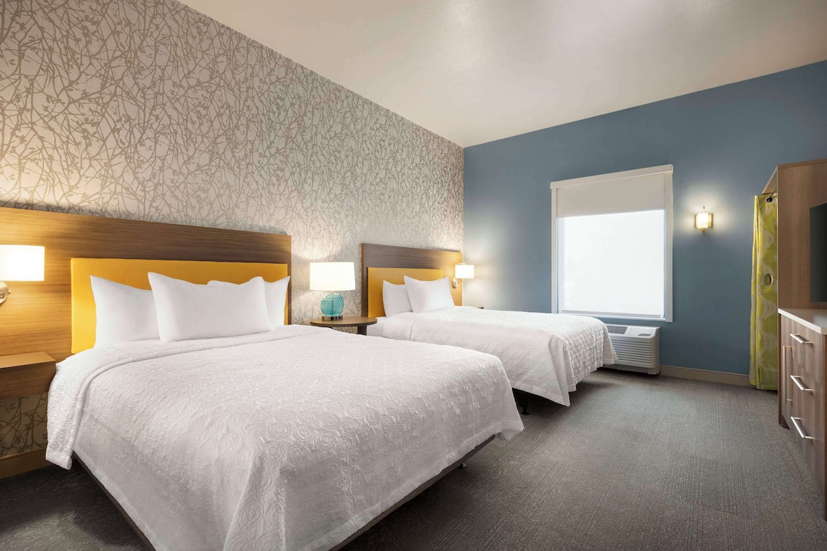 Een hotelkamer met twee bedden, een groot raam en een wand met een bloemenpatroon.